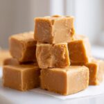 A close-up stack of creamy, light brown peanut butter fudge squares resting on parchment paper.