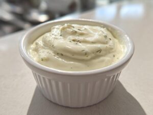 Close-up of creamy, homemade garlic aioli with visible herbs served in a small white fluted ramekin.