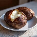 Two perfectly cooked air fryer baked potato halves sitting on a white plate, showing fluffy white insides.