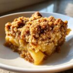 Close-up of a square serving of baked apple crisp recipe with a thick, crumbly topping on a white plate.