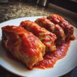 Four plump cabbage rolls generously covered in a rich, red tomato sauce, served on a white plate.