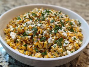 A close-up view of a white bowl filled with vibrant street corn salad featuring charred corn kernels, crumbled white cheese, and fresh cilantro.