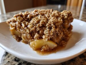 Close-up of a warm, gooey slice of apple crisp recipe with a thick, crumbly oat topping.