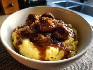 A close-up of a white bowl filled with creamy mashed potatoes topped with sausages and rich onion gravy, perfect for bangers and mash.