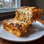 A slice of baked ravioli being lifted, showing extreme cheese pull and a browned, bubbly top layer.