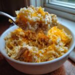 A spoonful of creamy crock pot chicken and rice topped with melted cheddar cheese being lifted from a white bowl.
