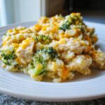 Close-up of a serving of creamy chicken broccoli rice casserole topped with melted cheddar cheese on a white plate.