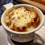 Close-up of a bowl of rich french onion soup topped with a crouton covered in bubbling, melted Gruyère cheese.