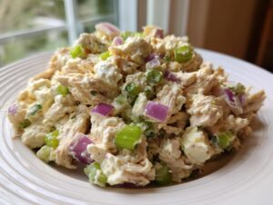A close-up of creamy cottage cheese chicken salad mixed with chunks of red onion and celery on a white plate.