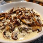 Close-up of rich, creamy mushroom sauce loaded with sautéed brown mushrooms and garnished with thyme.