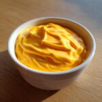 A close-up of thick, vibrant orange nacho cheese sauce swirled in a small white dipping bowl.