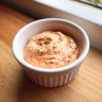 A close-up of thick, creamy remoulade sauce seasoned with herbs in a small white bowl.