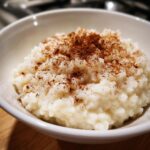 Close-up of creamy rice pudding served in a white bowl and generously sprinkled with ground cinnamon.