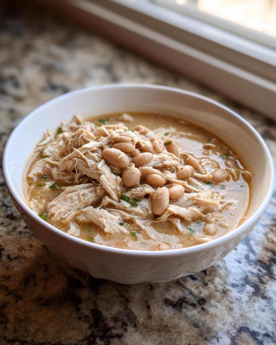 A white bowl filled with hearty crockpot white chicken chili, featuring shredded chicken and white beans in a creamy broth.