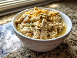 Close-up of a white bowl filled with shredded chicken, white beans, and melted cheese for crockpot white chicken chili.