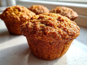 A close-up, featured image of a freshly baked honey bran muffin with a textured, golden-brown top, with others blurred in the background.