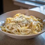 Close-up of fettuccine pasta generously coated in creamy homemade alfredo sauce and topped with herbs.