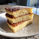 A close-up stack of three thick, fluffy almond flour pancakes dusted generously with powdered sugar.