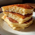 A stack of three incredibly fluffy pancakes cut in half, showing their airy texture and golden-brown edges.