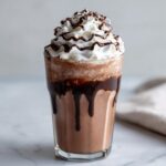 A tall glass of rich frozen hot chocolate drizzled with chocolate syrup and topped with whipped cream.