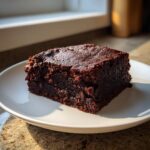 A close-up of a rich, dark, fudgy slice of sweet potato brownies on a white plate.