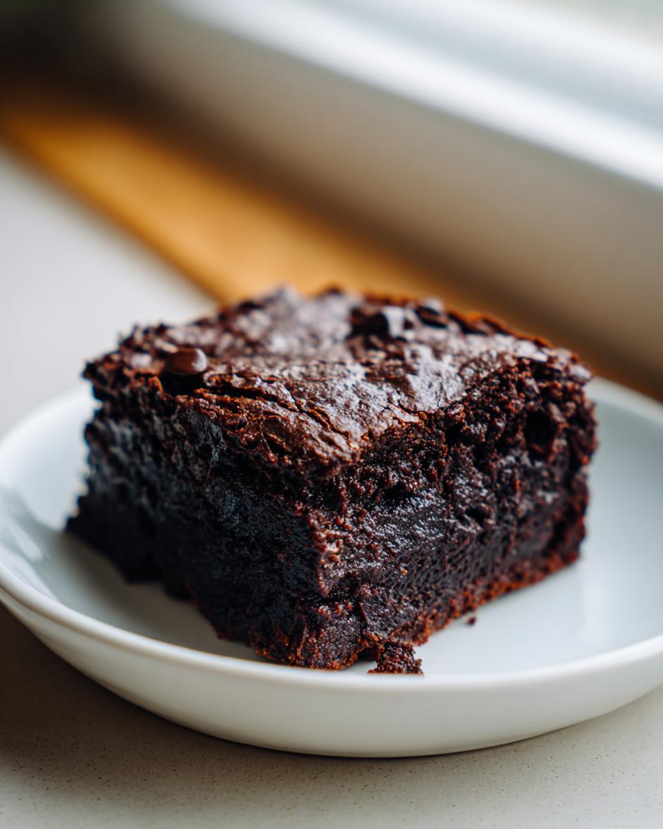Close-up of a single, rich, fudgy sweet potato brownie square topped with chocolate chips, served on a small white plate.