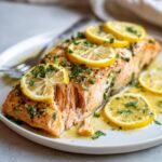 Close-up of a perfectly cooked salmon recipe fillet topped with lemon slices and fresh parsley in garlic butter sauce.