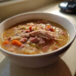 A close-up of a white bowl filled with rich Ham and Bean Soup, topped with shredded ham.