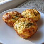 Three golden brown, savory egg bites topped with visible green herbs, resting on a white plate.