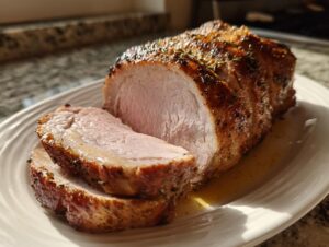 Close-up of a perfectly cooked, juicy pork loin roast, partially sliced, showing a pink interior and seasoned, browned exterior.