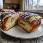 A slice of homemade King Cake, showing the cinnamon swirl filling and colorful Mardi Gras icing and sprinkles.