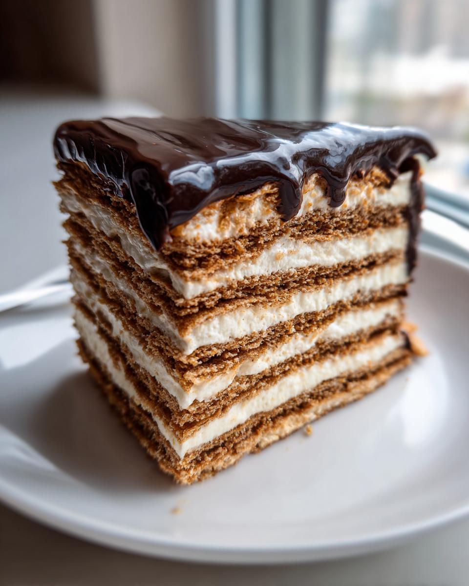 A tall, layered slice of chocolate eclair cake featuring multiple pastry layers and cream filling, topped with glossy chocolate ganache.
