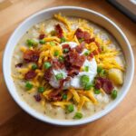 A bowl of creamy loaded baked potato soup topped with shredded cheese, bacon, sour cream, and green onions.
