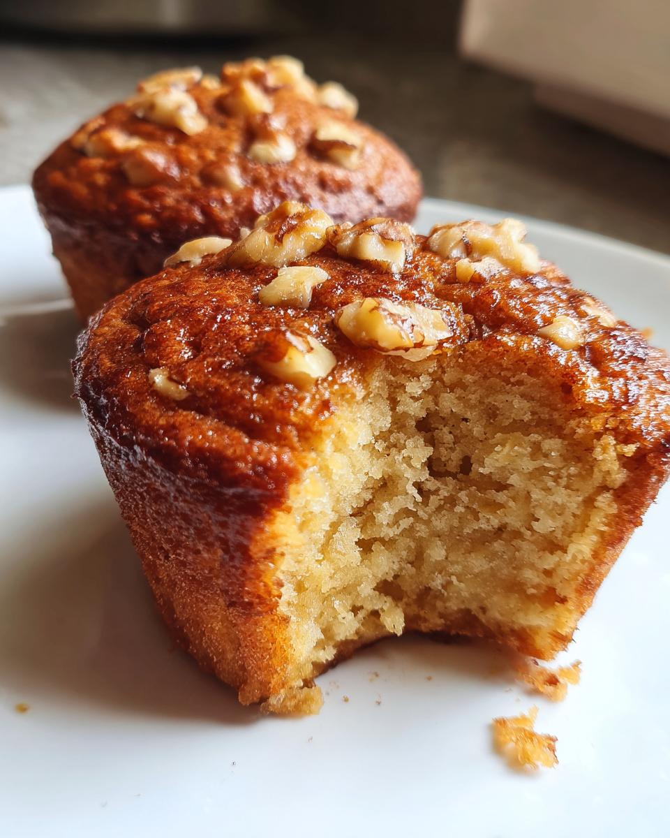 Close-up of a moist banana nut muffin with a bite taken out, showing the crumb texture and walnut topping.