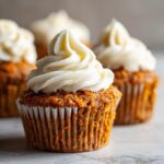 Close-up of a moist carrot cake muffin topped with a swirl of white cream cheese frosting.