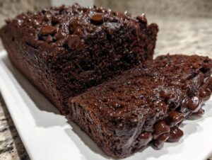 A close-up of rich, dark chocolate banana bread, sliced, showing melted chocolate chips on top.