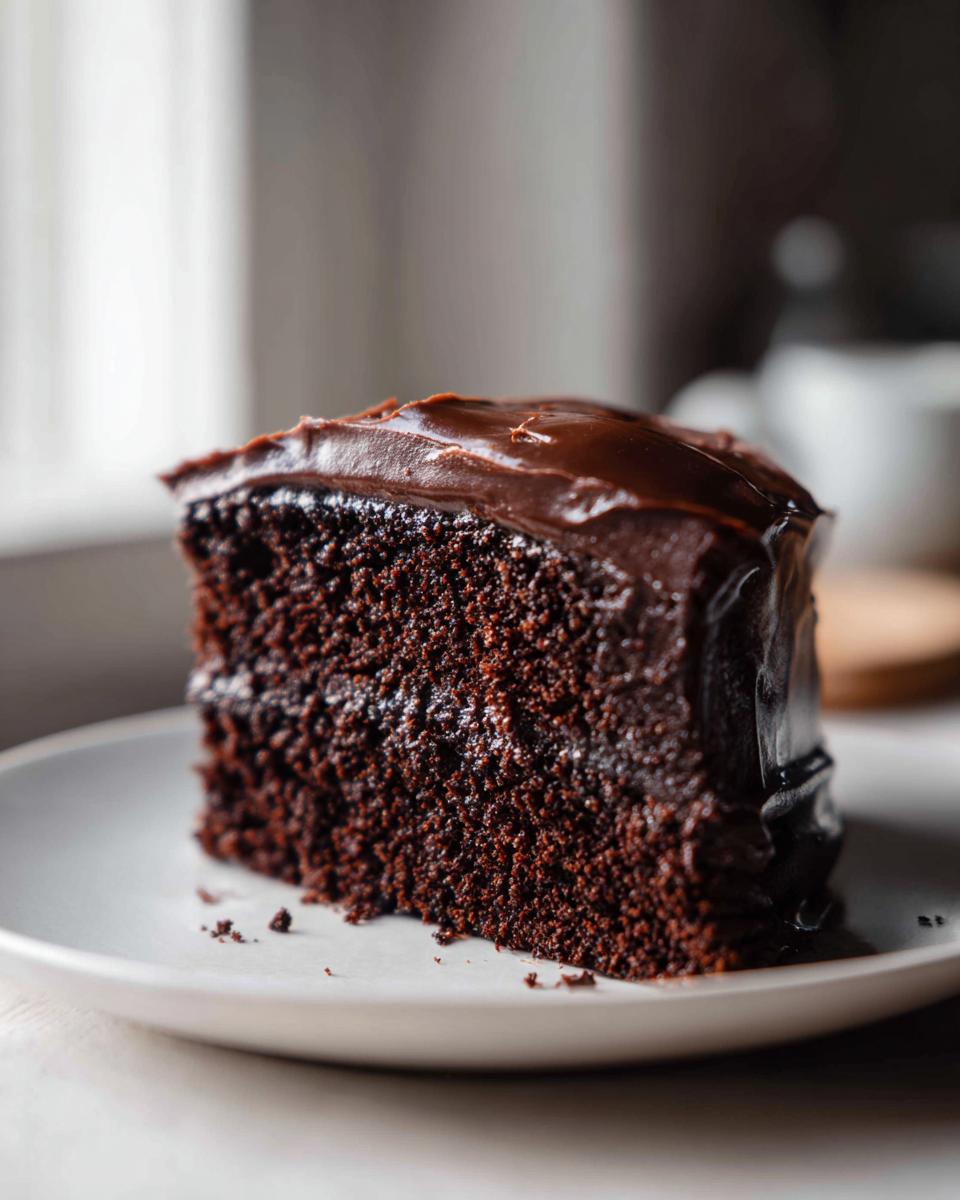 Close-up of a decadent slice of moist chocolate cake topped with glossy dark chocolate frosting.