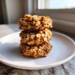 Three dense, oatmeal-based breakfast cookie power bites stacked vertically on a white plate.