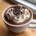 Close-up of a mug filled with rich hot chocolate, topped generously with whipped cream and dark chocolate shavings.