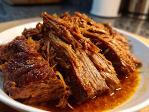 Close-up of tender, shredded Mississippi pot roast served in its rich, savory sauce on a white bowl.