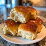 A stack of incredibly soft, golden-brown dinner rolls glistening with a sweet glaze, one roll pulled apart to show the fluffy interior.