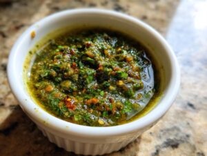 Close-up of vibrant, chunky green tomato salsa seasoned with herbs and chili flakes in a small white bowl.