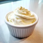 A close-up of freshly whipped, creamy garlic aioli served in a small white fluted ramekin.
