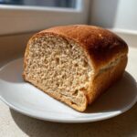 A half loaf of homemade whole wheat bread with a golden-brown crust, showing a soft, textured crumb.