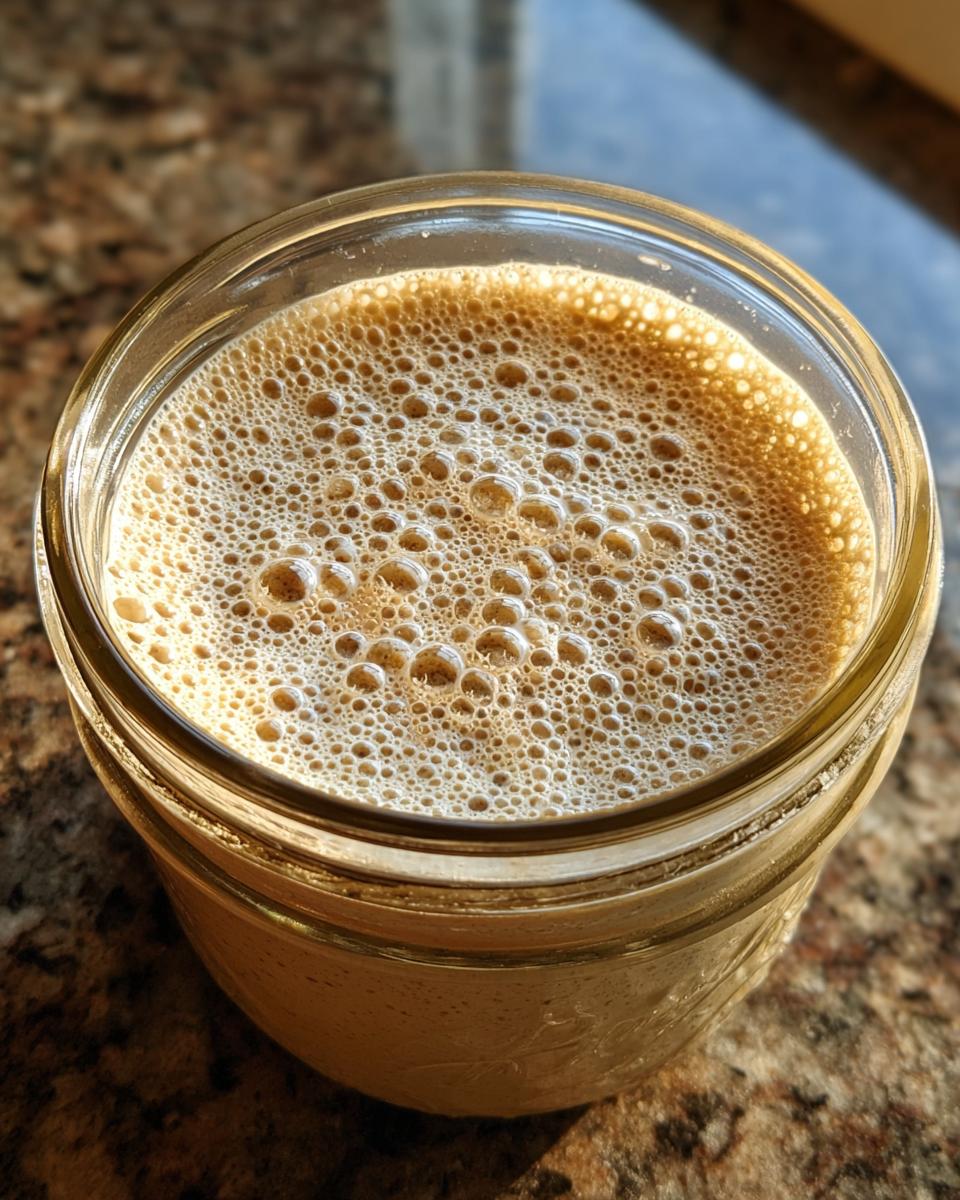 Close-up of an active sourdough starter in a glass jar, showing a thick layer of small, active bubbles.