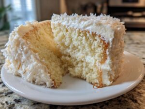 Close-up of two slices of moist coconut cake layered with white frosting and covered in shredded coconut.