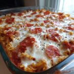 Close-up of a bubbling pizza casserole topped with melted mozzarella, pepperoni slices, and herbs.