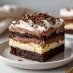 A decadent slice of brownie refrigerator cake showing layers of dark brownie, cream filling, chocolate mousse, and whipped topping.