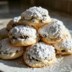A tempting stack of freshly baked cannoli cookies heavily dusted with powdered sugar, showing chocolate chips inside.