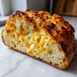 Cross-section of a thick slice of cheesy egg toast showing a fluffy interior and golden-brown, bubbly cheese topping.